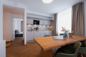 A modern kitchen with white cabinets, a microwave, and a coffee maker. There is a dining table with chairs and a vase of flowers.