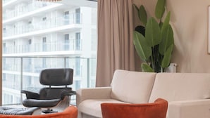Un salon moderne avec un canapé, deux fauteuils, une grande plante et une vue sur un immeuble de grande hauteur.