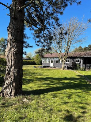 A house with a large tree in the foreground, a well-maintained lawn, and a clear blue sky.