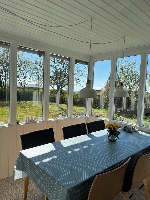 Un coin repas avec une table dressée pour quatre personnes, de grandes fenêtres et une vue sur une cour verdoyante.