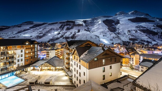 Ein schneebedeckter Berg bei Nacht mit einem hellen Stern am Himmel. Im Vordergrund befinden sich Gebäude mit Balkonen und ein Poolbereich.