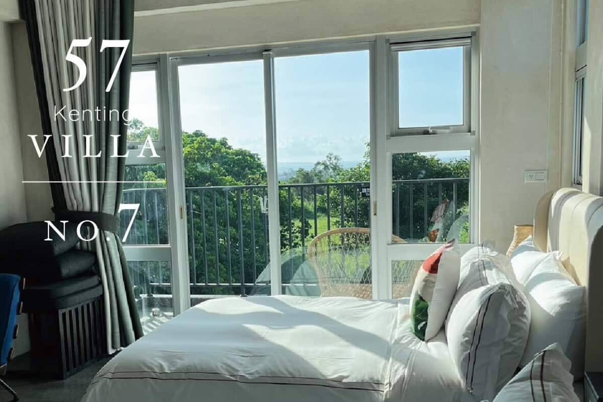 Un dormitorio con una cama grande, una silla y vistas a zonas verdes a través de amplios ventanales.