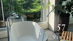 A modern bathroom with a freestanding bathtub, large windows offering a view of lush greenery, and a potted plant. - 57villa (Hengchun)