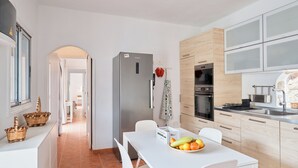 Eine moderne Küche mit weißen Schränken, einem Edelstahl-Kühlschrank und einem Essbereich mit weißem Tisch und Stühlen.