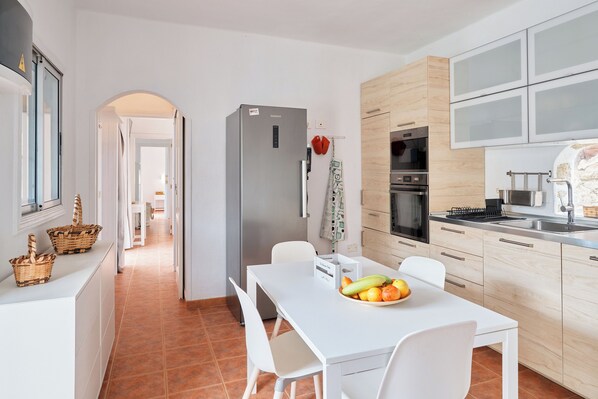 Eine moderne Küche mit weißen Schränken, einem Edelstahl-Kühlschrank und einem Essbereich mit weißem Tisch und Stühlen.