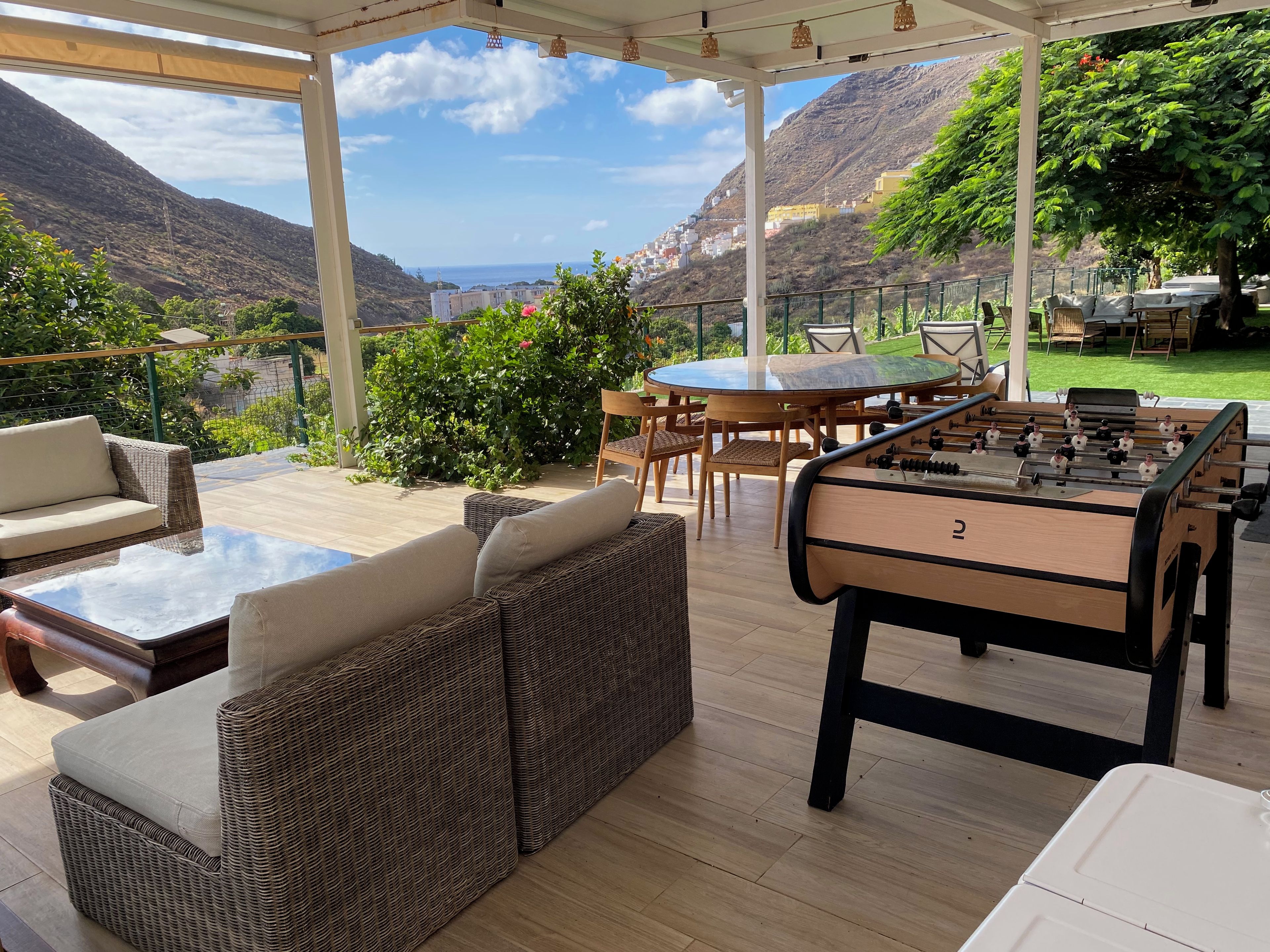 Une terrasse extérieure avec une table de baby-foot, des meubles en osier et une vue sur la mer et les collines.