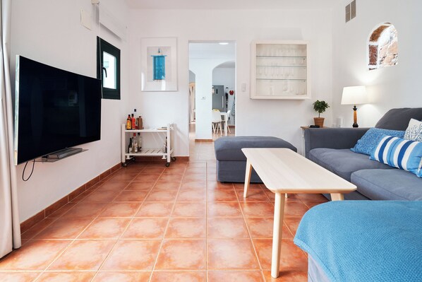 Ein Wohnzimmer mit Flachbildfernseher, einer Couch, einem Couchtisch und einem Essbereich mit Stühlen.