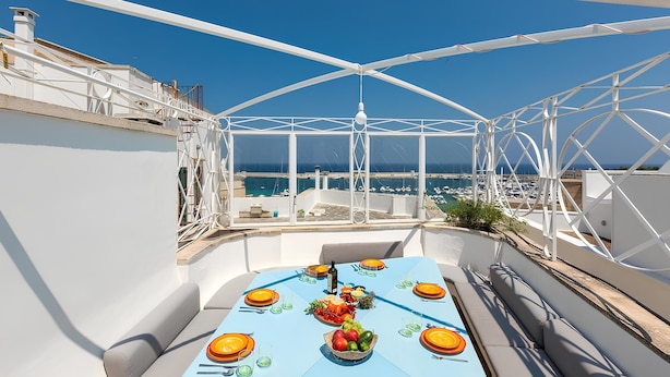A rooftop terrace with a table set for dining, overlooking a coastal cityscape. - Dimora Storica Torre Matta – Elegance, history and sea views in the heart of Otr (Otranto)