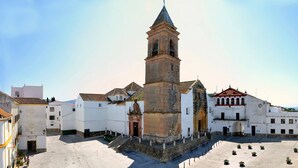 Una plaza histórica con una iglesia destacada que cuenta con un campanario, rodeada de edificios tradicionales con tejados de tejas.