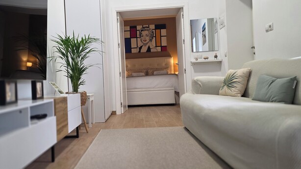Una sala de estar moderna con sofá, televisor, planta y cama con un cuadro de colores.