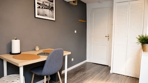 Una stanza con un tavolo da pranzo, una sedia, un quadro appeso al muro, una porta bianca e una piccola pianta.