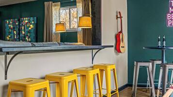 A room with a bed, yellow stools, a guitar, and a table with bottles.