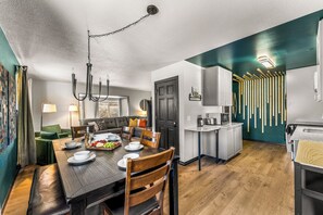 A modern kitchen with a dining area, wooden flooring, and a black door.