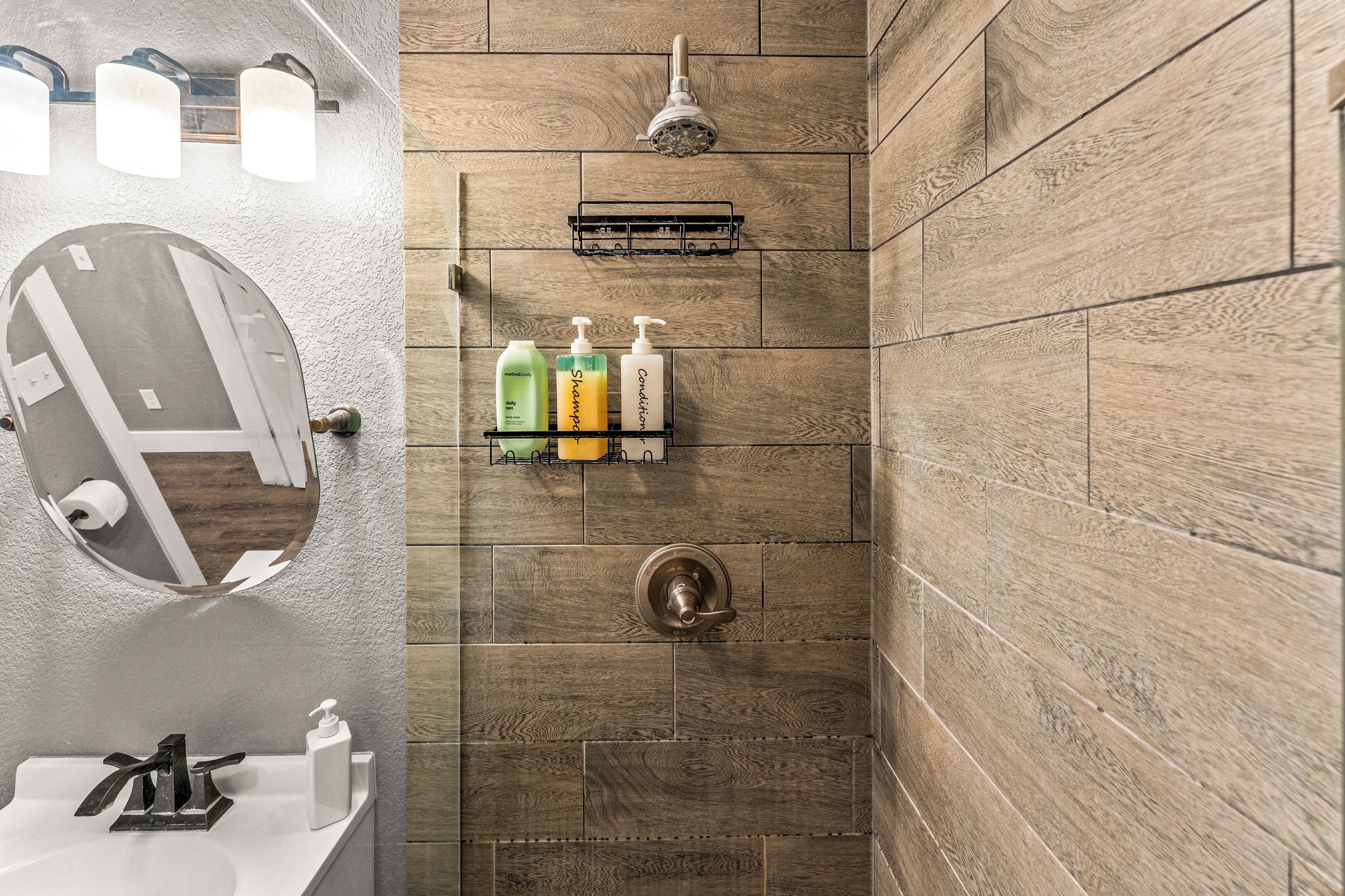 Un baño con pared de madera, ducha, lavamanos y artículos de aseo en un estante.