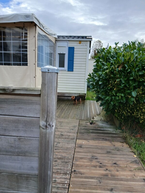 A wooden deck leading to a house with a blue shutter and a covered porch.