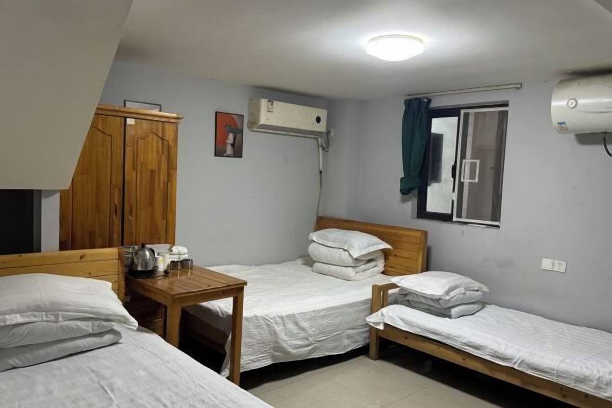 A small, well-lit room with two single beds, a wooden table, and a wardrobe.