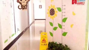 A hallway with a yellow caution sign, a sunflower mural, and a red carpet. - Oushang Apartment (Shanghai)