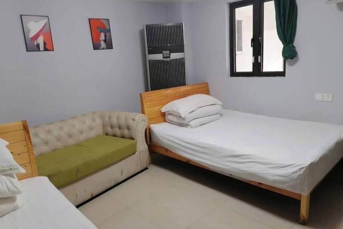 A bedroom with a bed, a sofa, a window, and an air conditioning unit.