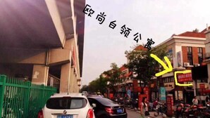 A street scene with buildings, a white car, and a green fence. - Oushang Apartment (Shanghai)