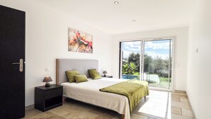 Een slaapkamer met een bed, nachtkastje, schilderij en uitzicht op een zwembad door een schuifdeur.
