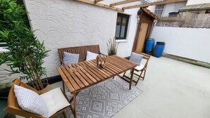 A wooden table and chairs set on a patterned rug, with a white textured wall and a wooden pergola overhead. - Charming half-timbered house in the heart of the city! "Fachwerkstube" (Witzenhausen)