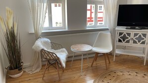 A modern living room with a white TV stand, a white chair, a small round table, and a large potted plant. - Charming half-timbered house in the heart of the city! "Fachwerkstube" (Witzenhausen)