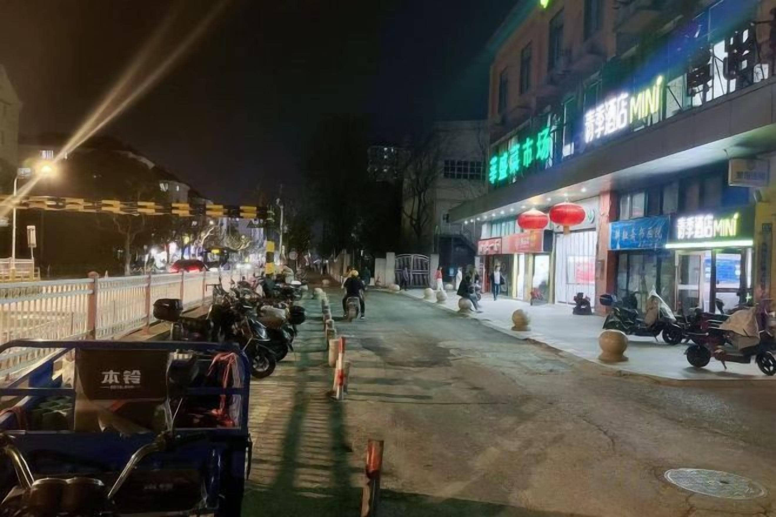 Una calle iluminada de noche con motocicletas estacionadas, escaparates iluminados y una acera para peatones.
