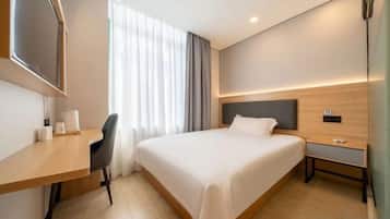 Una habitación de hotel con cama, escritorio, silla, televisor y ventana con cortinas.