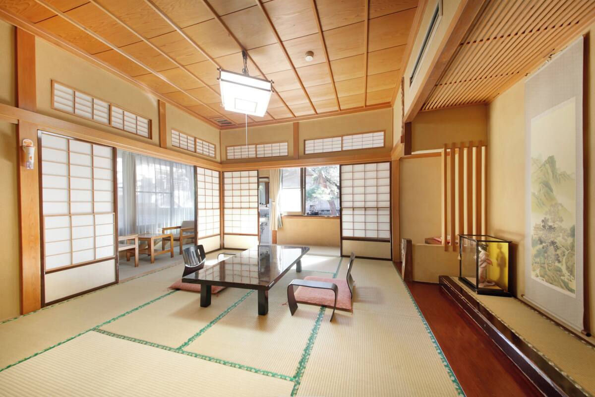 Une pièce de style japonais traditionnel, avec un sol recouvert de tatamis, des portes coulissantes, une petite table basse et une œuvre d’art encadrée accrochée au mur.