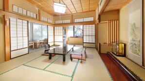 Een traditionele Japanse kamer met tatami vloerbedekking, schuifdeuren, een lage tafel en een kunstwerk in een lijst aan de muur.