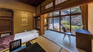 Een traditionele Japanse kamer met tatami vloeren, een bed, een bureau en uitzicht op de tuin.