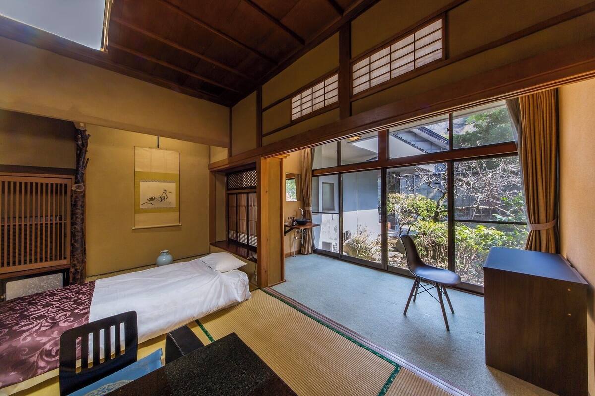 Une pièce de style japonais traditionnel, avec un sol recouvert de tatamis, un lit, un bureau et une vue sur le jardin.