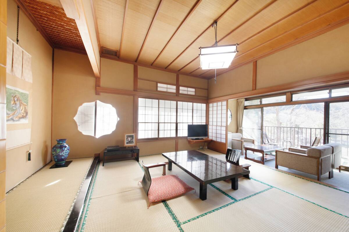 Une pièce de style japonais traditionnel, avec un sol recouvert de tatamis, une table basse, un canapé et de grandes fenêtres.