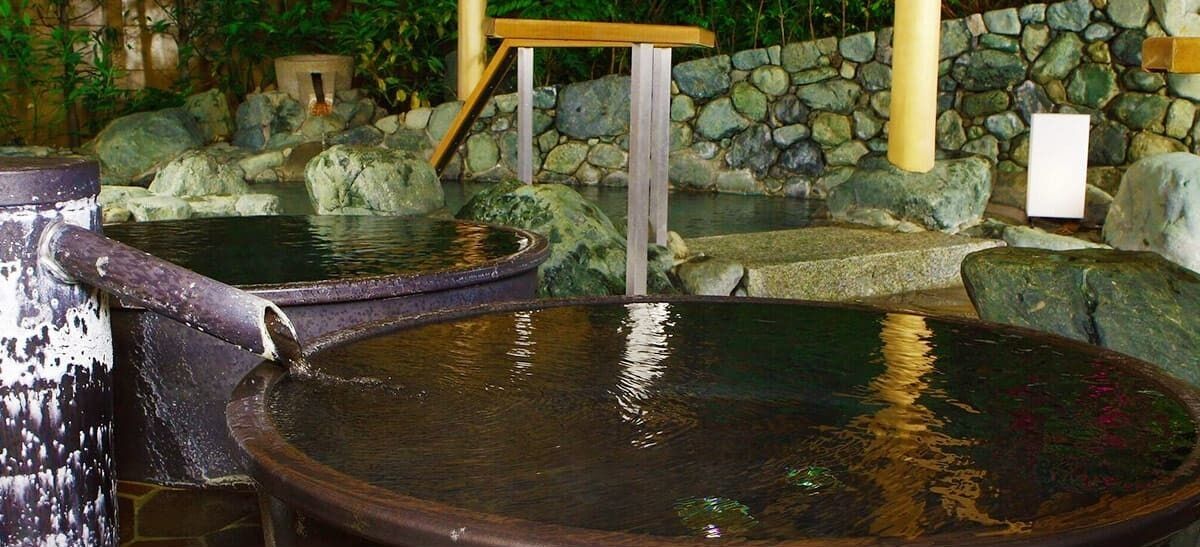 Un onsen japonés tradicional con bañeras de piedra y un banco de madera.