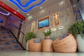 A lobby with a marble wall, a TV, and wicker seating. - Baolihua Hotel (Shanghai)