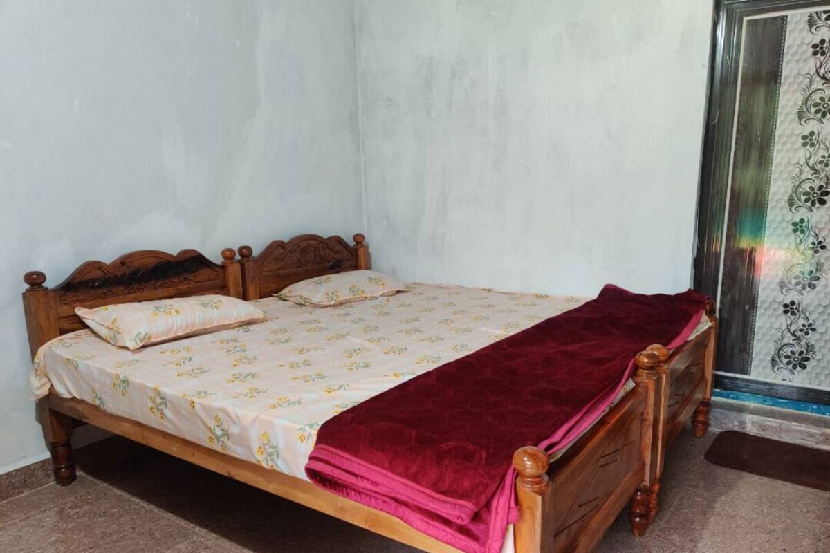 Una cama de madera con una colcha estampada y una manta roja, un cabecero de madera, y una puerta con un panel de vidrio decorativo.
