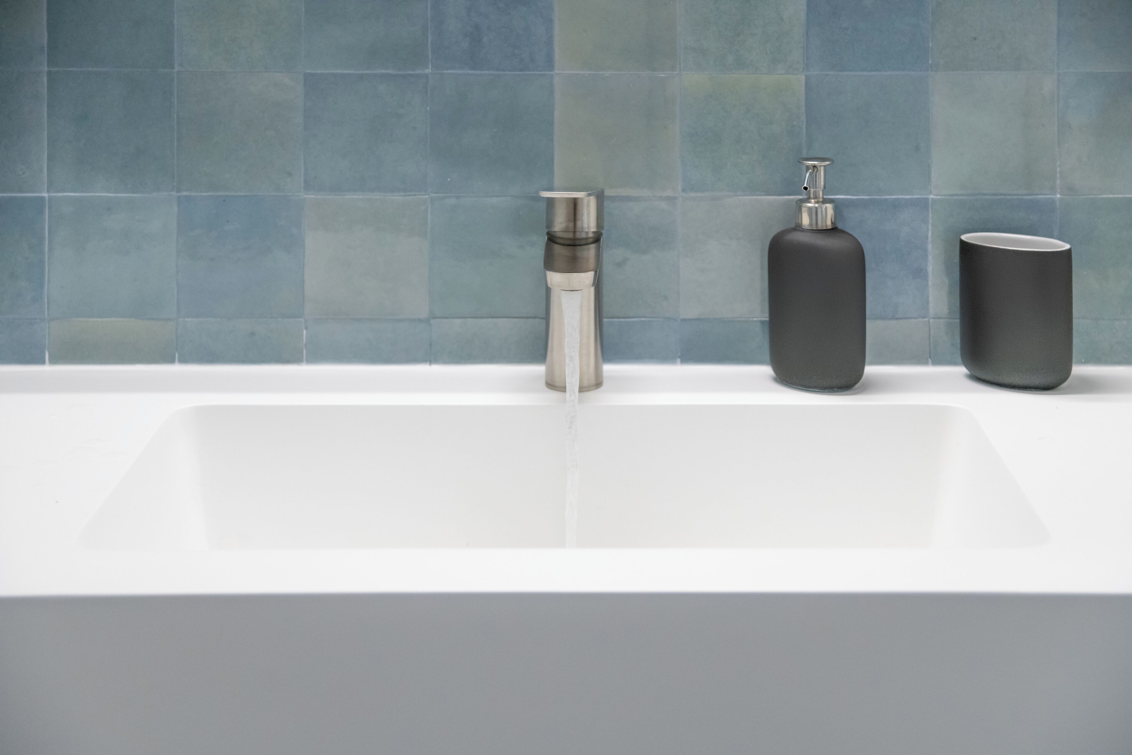 A bathroom with a white sink, a metallic soap dispenser, and a black soap bottle.