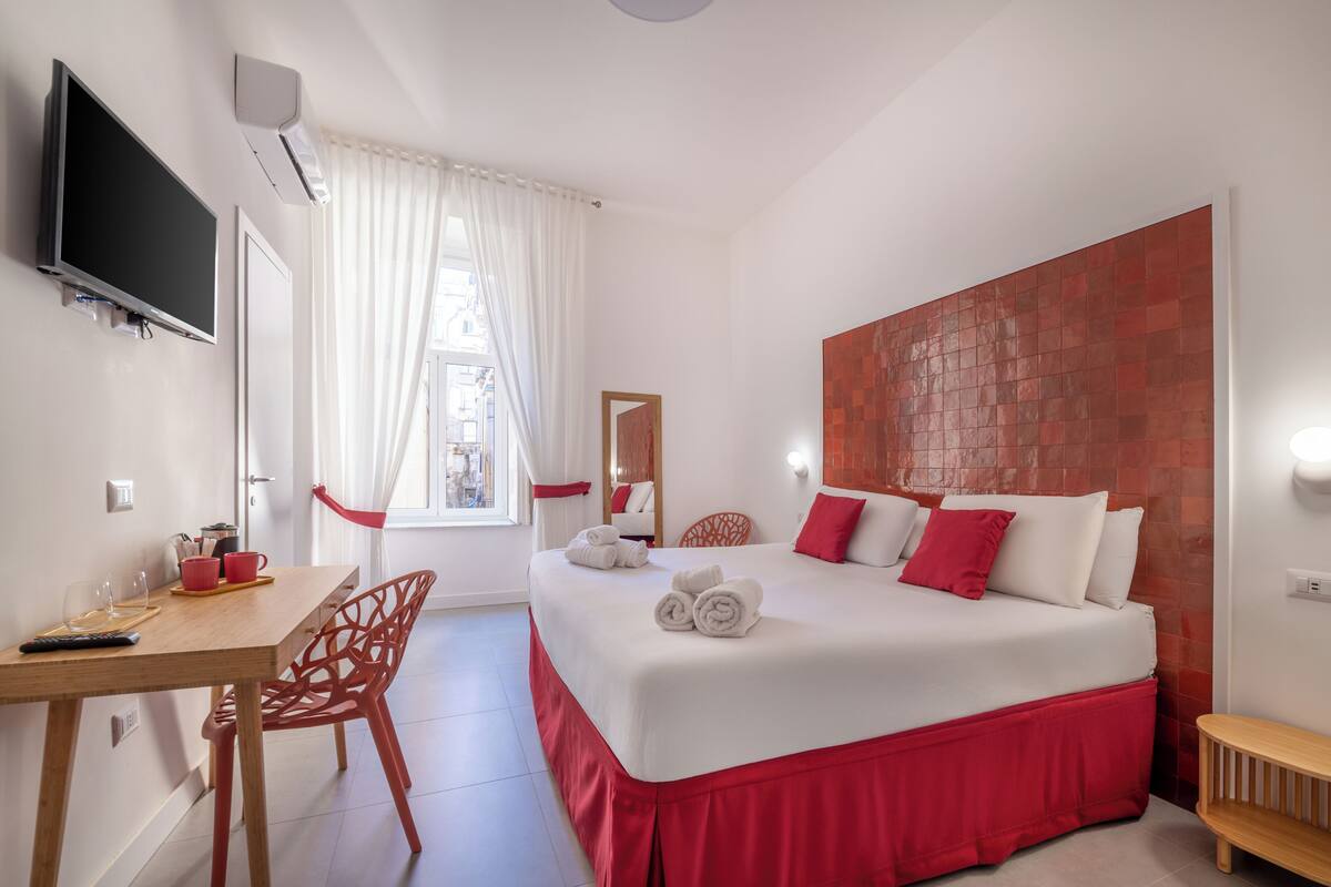 A hotel room with a bed, a desk with a chair, a TV, and a window with curtains.