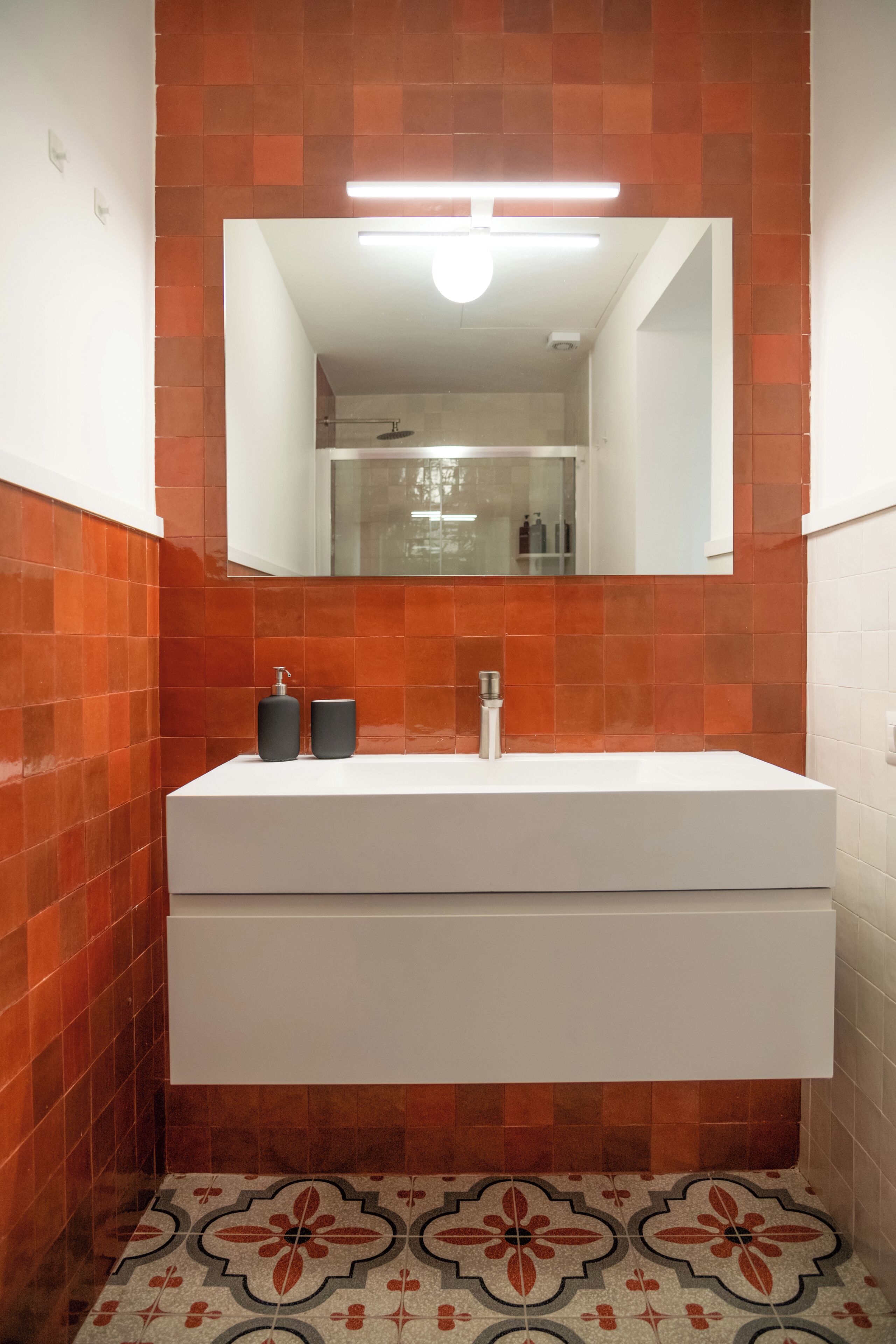 A bathroom with a white vanity, orange-tiled walls, and patterned floor tiles.