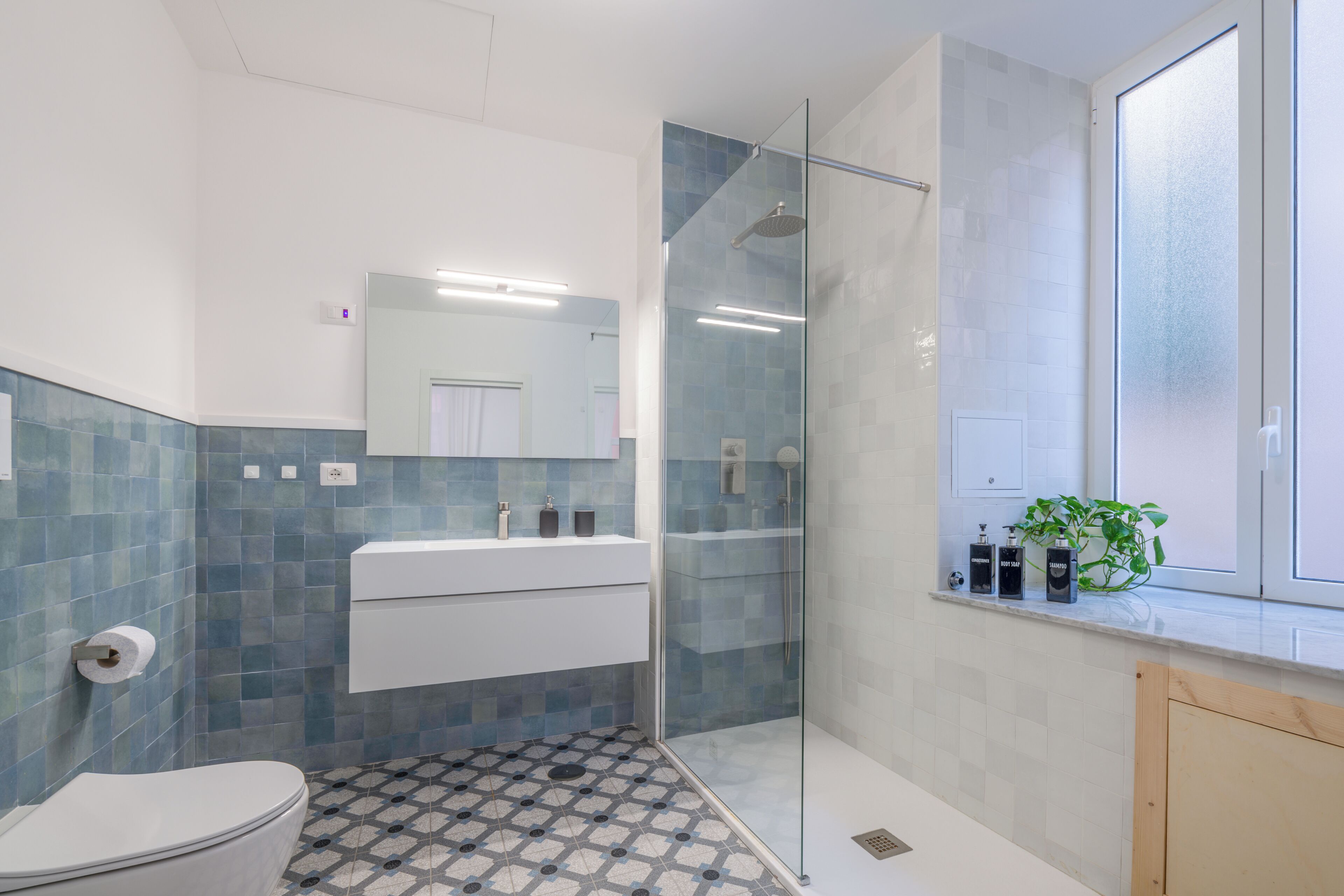 A modern bathroom with a glass-enclosed shower, a white sink, and a patterned floor.