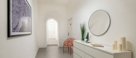 A modern hallway with a framed artwork, a round mirror, a white console table with candles, and a red chair.