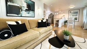 Una sala de estar moderna con un sofá color beige, cojines blancos y negros, una mesa de centro con una planta y un cuadro abstracto grande sobre el sofá.