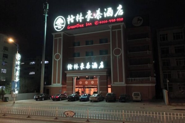 A hotel with a prominent sign, multiple floors, and a parking lot with several cars.