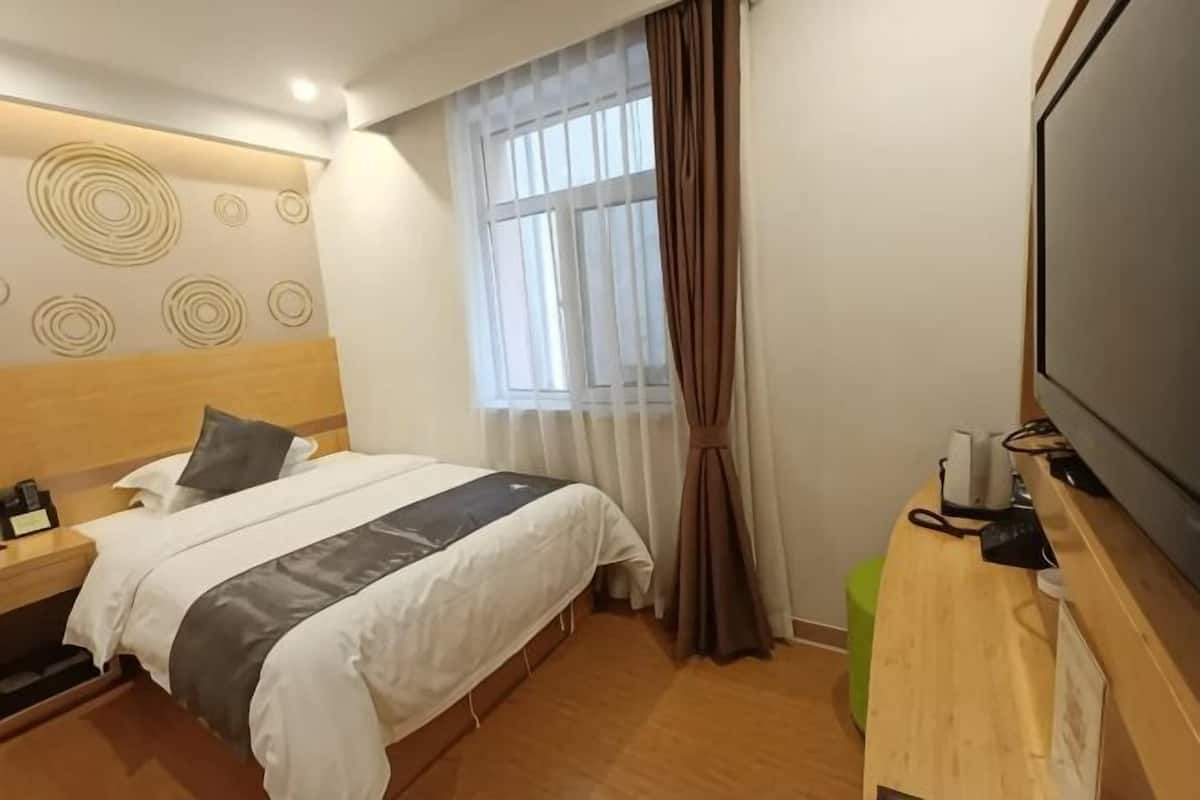 A hotel room with a bed, a wooden headboard, a TV, a desk, and a window with curtains.