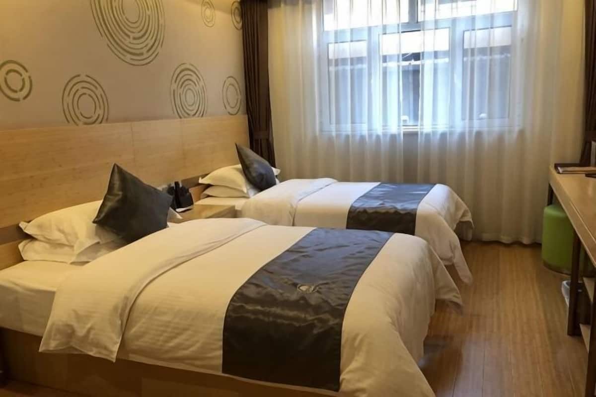 Two beds with headboards, a wooden floor, a window with curtains, and a wall with circular patterns.