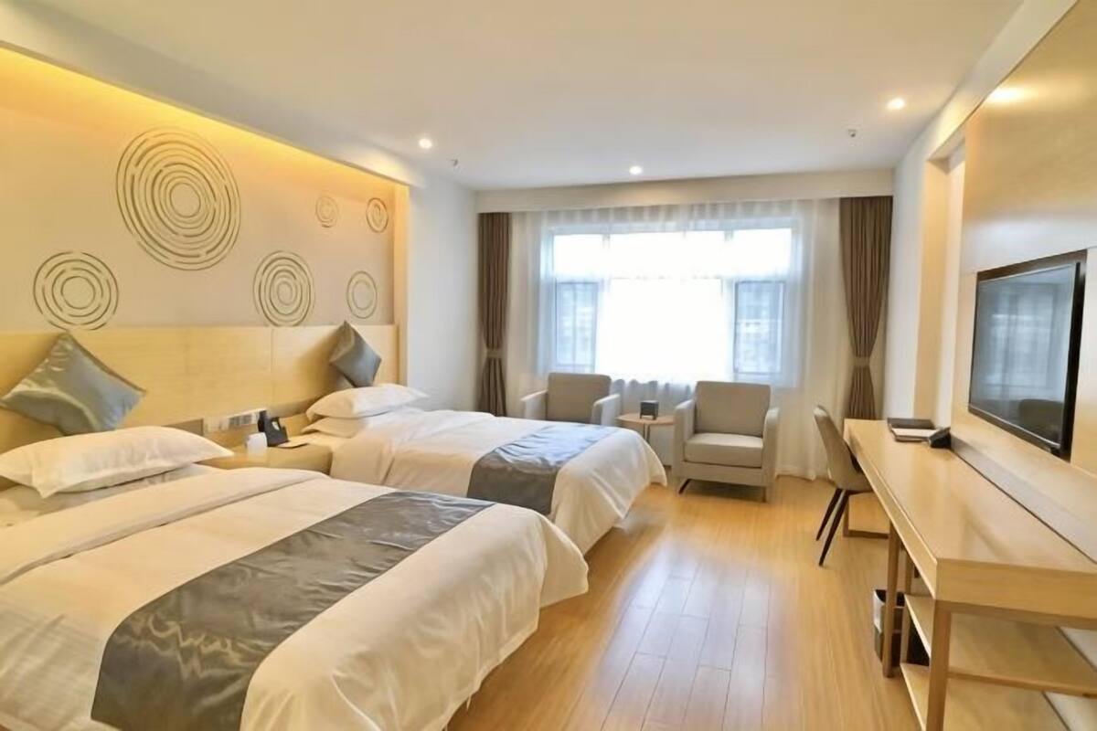A hotel room with two beds, a desk, a TV, and a large window.