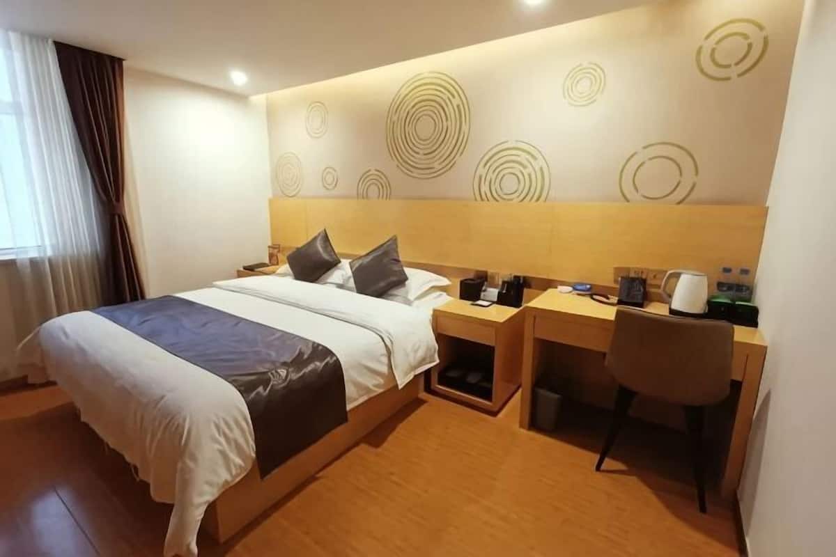 A hotel room with a bed, a desk, a chair, a nightstand, and a wall with circular patterns.