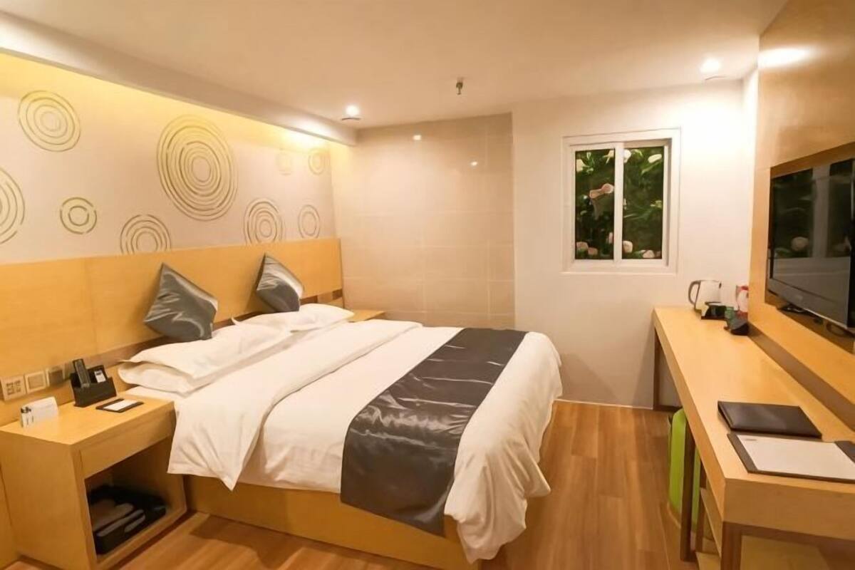 A modern hotel room with a bed, bedside table, desk, and TV.
