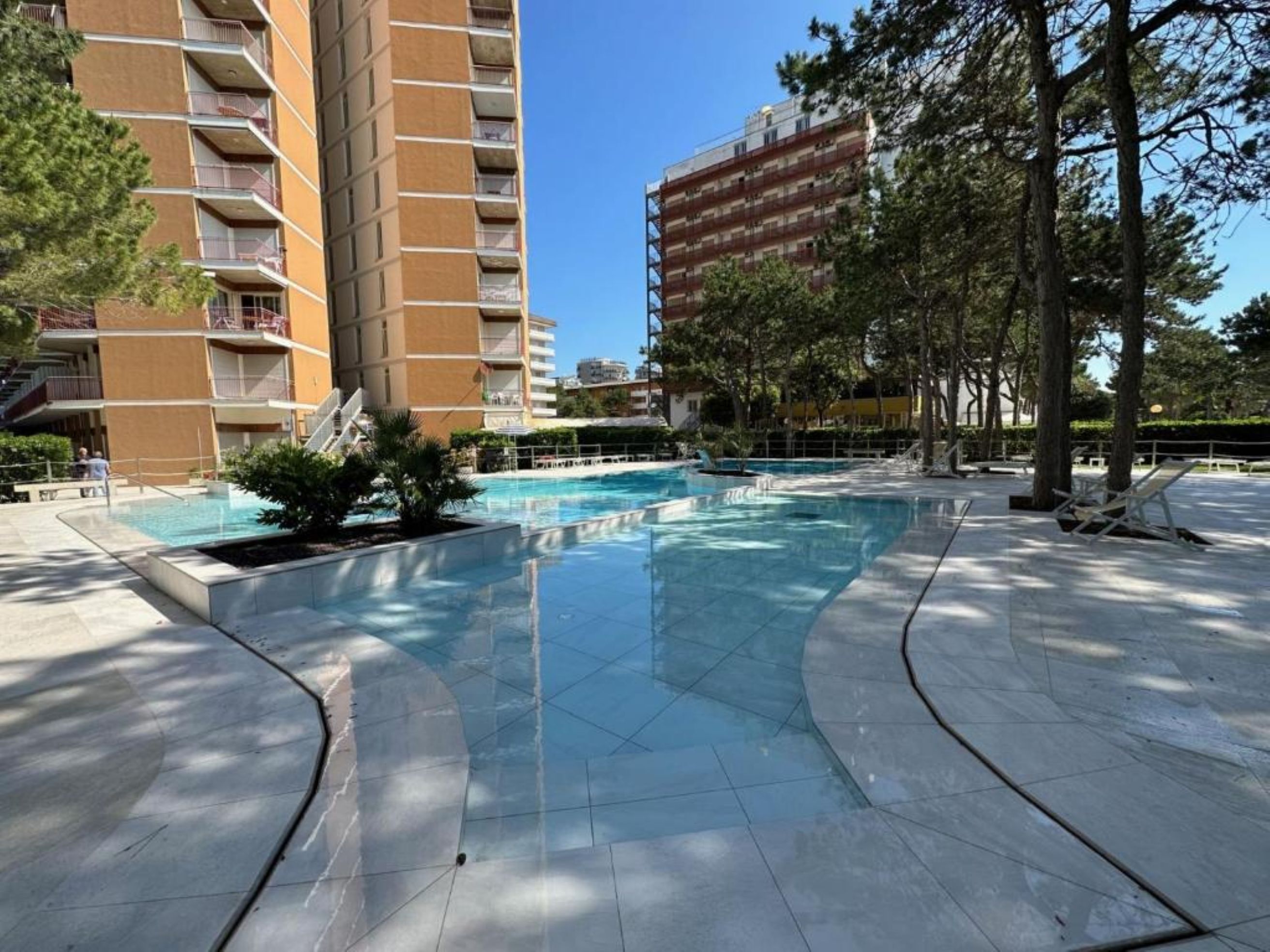 Piscina rodeada por um deck revestido com azulejos, com um edifício alto ao fundo.