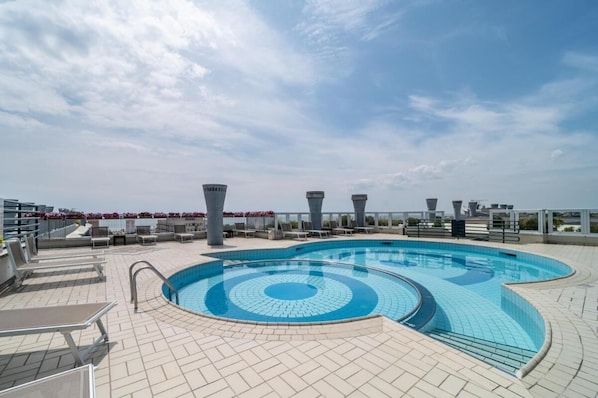 A rooftop pool with a circular design, lounge chairs, and a clear sky.